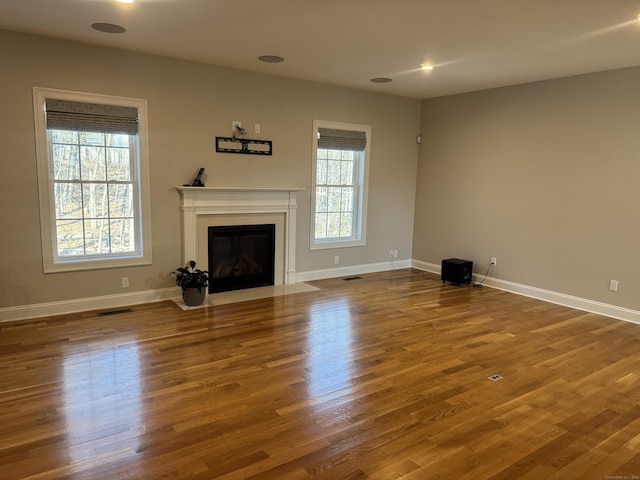 unfurnished living room with wood finished floors, visible vents, baseboards, a fireplace with flush hearth, and recessed lighting