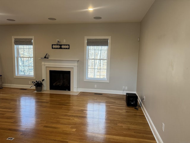 unfurnished living room with a fireplace with flush hearth, visible vents, baseboards, and wood finished floors