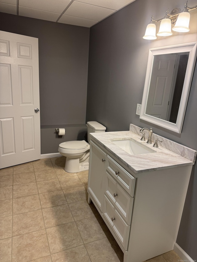 half bath featuring vanity, baseboards, a drop ceiling, tile patterned flooring, and toilet