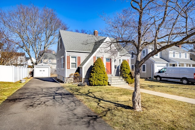 view of front of house with an outbuilding, a front yard, fence, a residential view, and driveway