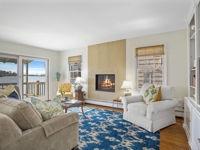 living area with a baseboard radiator, a large fireplace, wood finished floors, and a water view