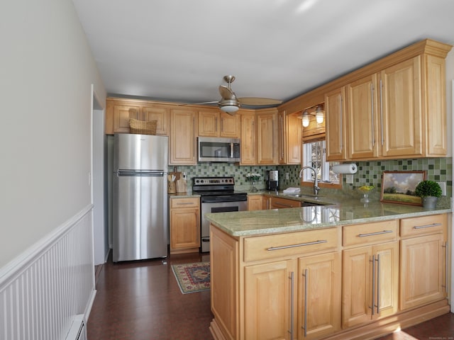 kitchen with light stone countertops, wainscoting, appliances with stainless steel finishes, a peninsula, and a sink