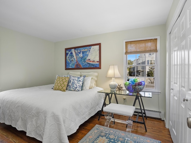 bedroom featuring a baseboard heating unit, wood finished floors, and a closet