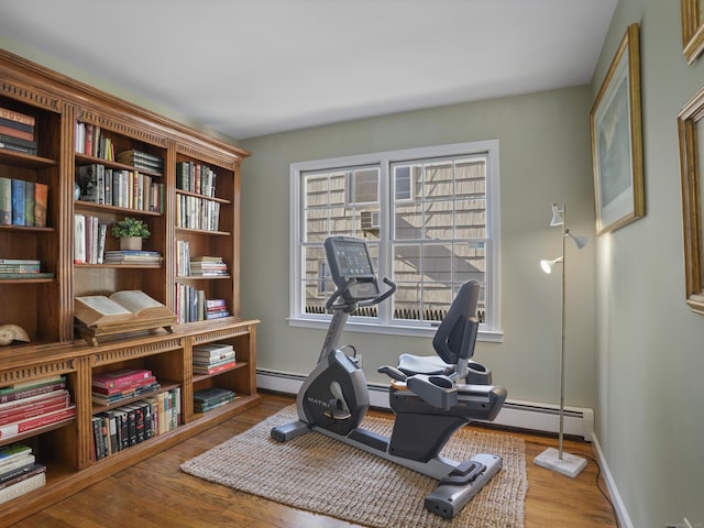 exercise room featuring a baseboard radiator, baseboards, and wood finished floors