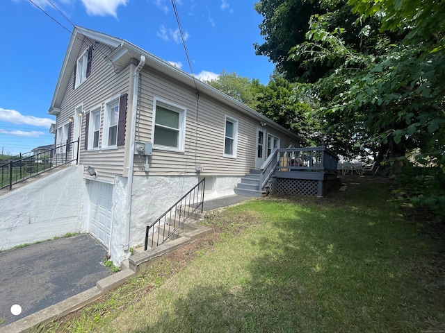 view of side of home with a garage, a yard, a wooden deck, and driveway