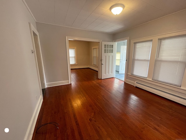 empty room featuring a baseboard heating unit, wood finished floors, and baseboards