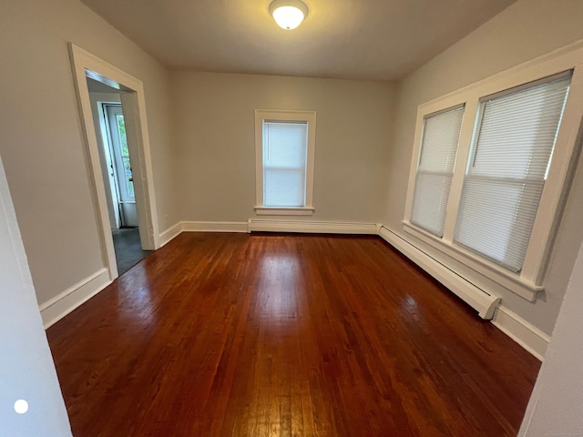 empty room with a baseboard heating unit, baseboards, and dark wood-style floors