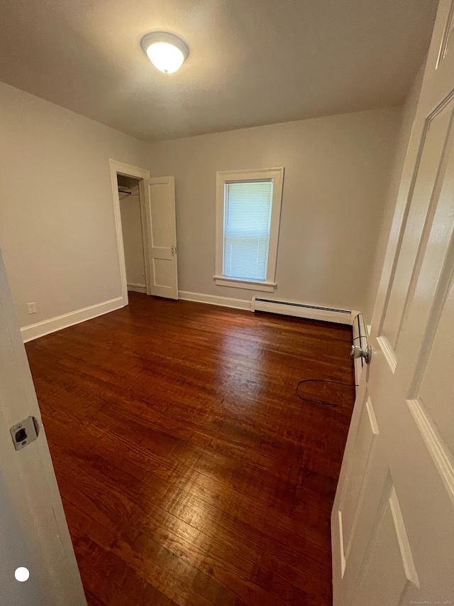 unfurnished bedroom with dark wood-style floors, baseboards, and baseboard heating