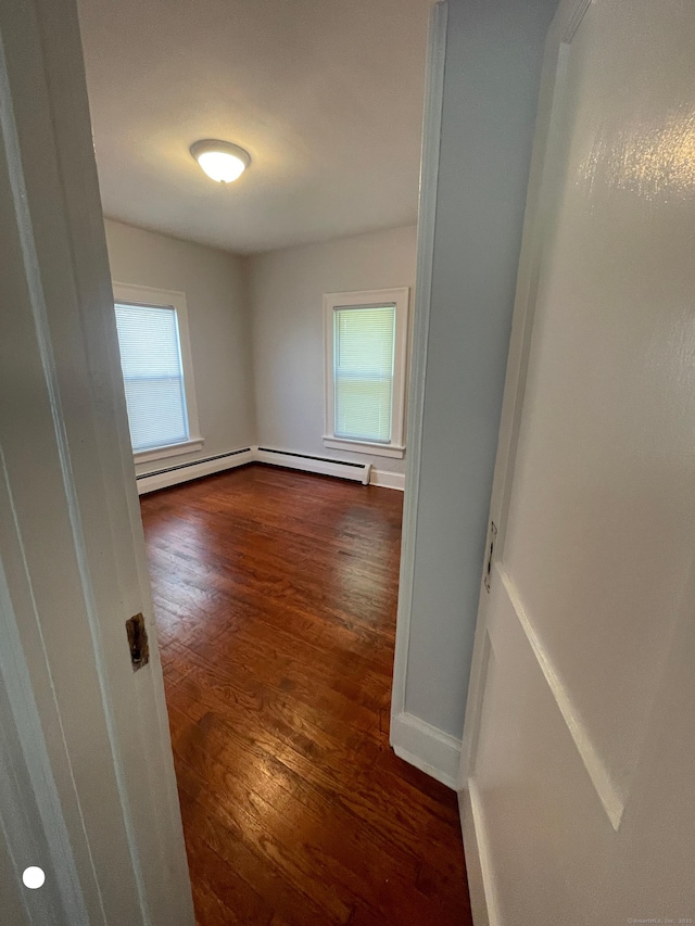 spare room with dark wood-style floors, a baseboard heating unit, plenty of natural light, and baseboards