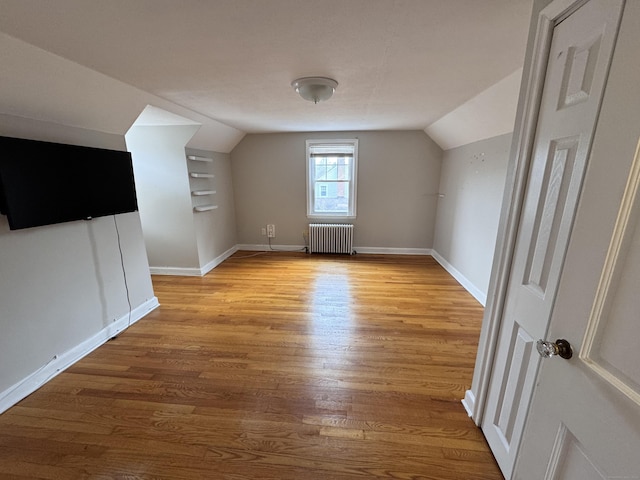 additional living space featuring light wood-type flooring, radiator heating unit, baseboards, and vaulted ceiling