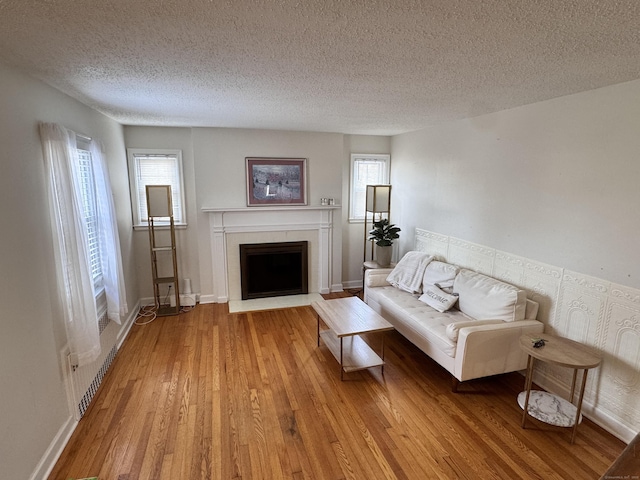 unfurnished living room featuring light wood-style floors, baseboards, a textured ceiling, and a fireplace with flush hearth