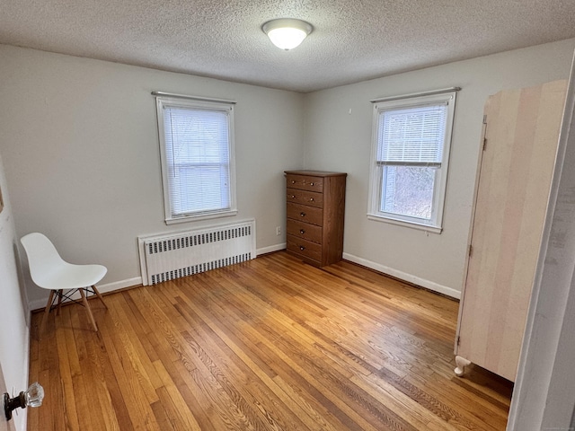 interior space featuring radiator, light wood-type flooring, baseboards, and a textured ceiling