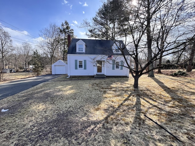 cape cod house with entry steps, an outbuilding, aphalt driveway, a detached garage, and a chimney