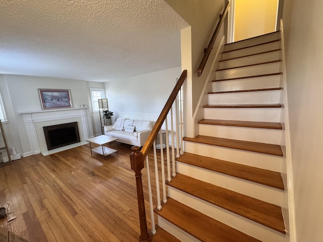 staircase with a textured ceiling, hardwood / wood-style floors, and a fireplace with flush hearth