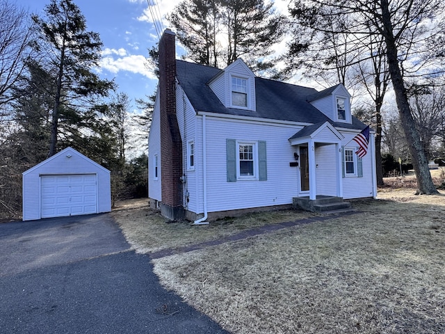 cape cod house featuring a garage, driveway, a chimney, and an outbuilding