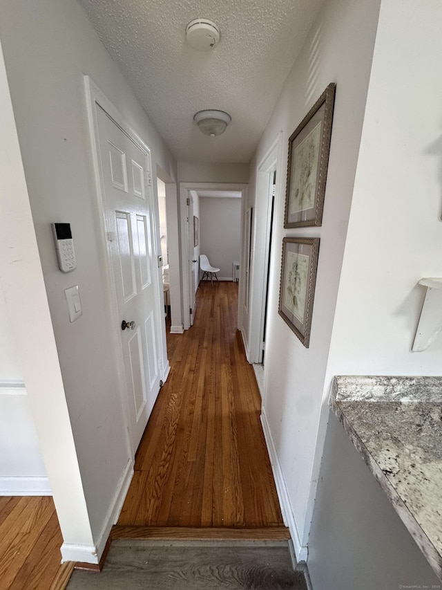 corridor with baseboards, a textured ceiling, and wood finished floors