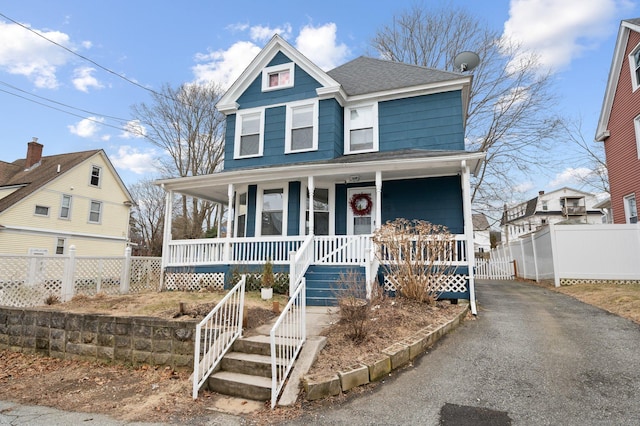 view of front of house with covered porch, driveway, a shingled roof, and fence