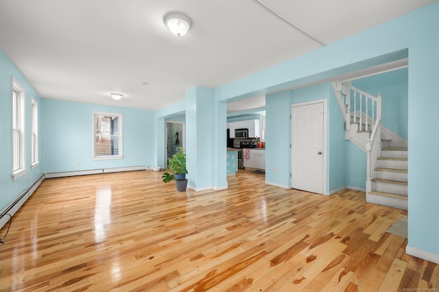 empty room featuring baseboard heating, baseboards, light wood finished floors, and stairs