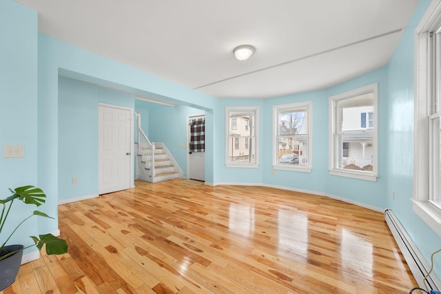 spare room with light wood-type flooring, a baseboard radiator, stairway, and baseboards