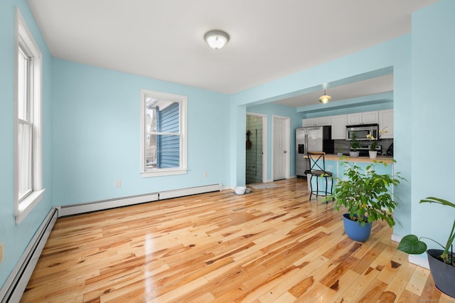 living room featuring baseboard heating, light wood-type flooring, and a wealth of natural light