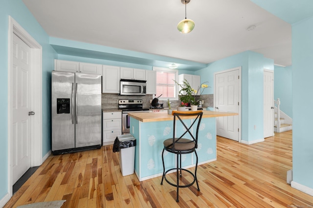 kitchen with light wood finished floors, butcher block counters, appliances with stainless steel finishes, a center island, and backsplash