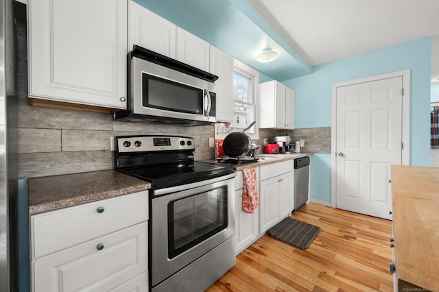 kitchen featuring light wood-style floors, appliances with stainless steel finishes, white cabinets, and decorative backsplash