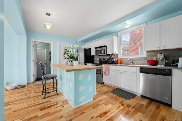 kitchen with light wood finished floors, butcher block countertops, a sink, stainless steel appliances, and backsplash