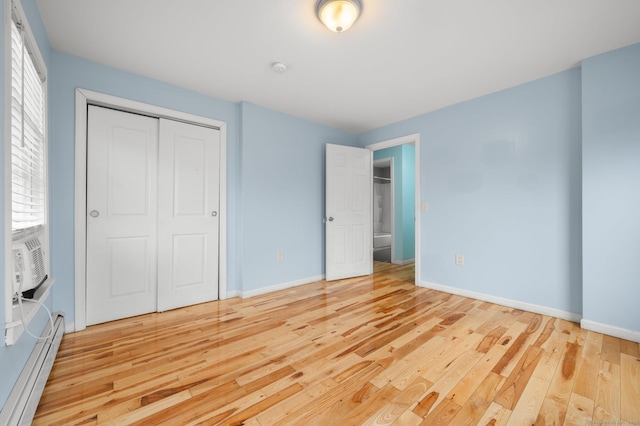 unfurnished bedroom with a closet, a baseboard radiator, wood-type flooring, and baseboards