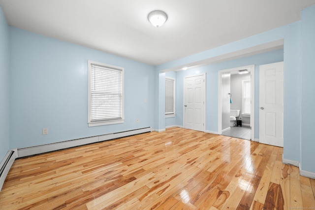 unfurnished bedroom featuring wood-type flooring, baseboards, baseboard heating, and ensuite bathroom