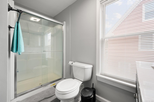 bathroom with a stall shower, a healthy amount of sunlight, and toilet