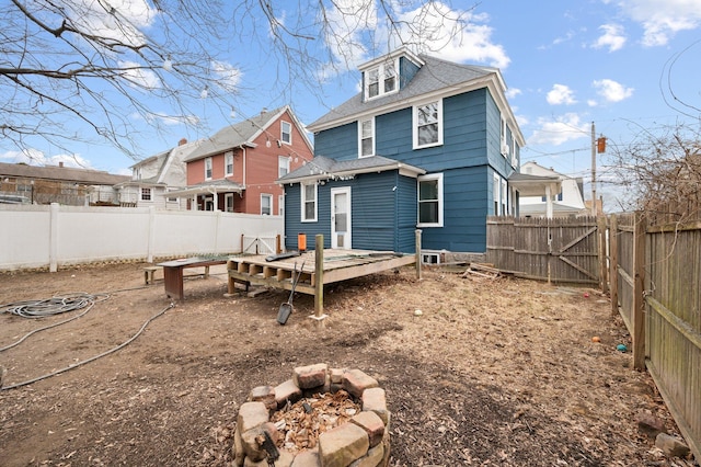 back of house featuring a deck, an outdoor fire pit, roof with shingles, and a fenced backyard