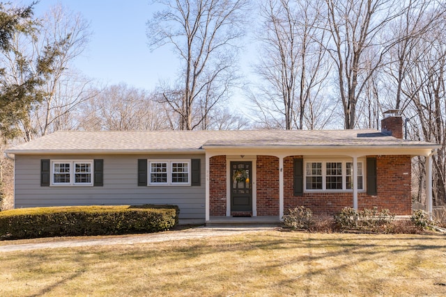 view of front of property with a front yard, a porch, brick siding, and a chimney