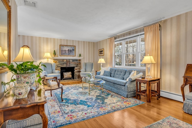 living area featuring visible vents, a stone fireplace, wood finished floors, and a baseboard radiator