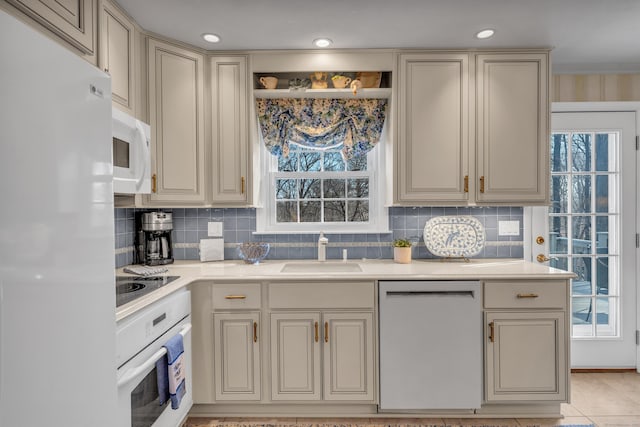 kitchen featuring cream cabinetry, white appliances, light countertops, and a sink