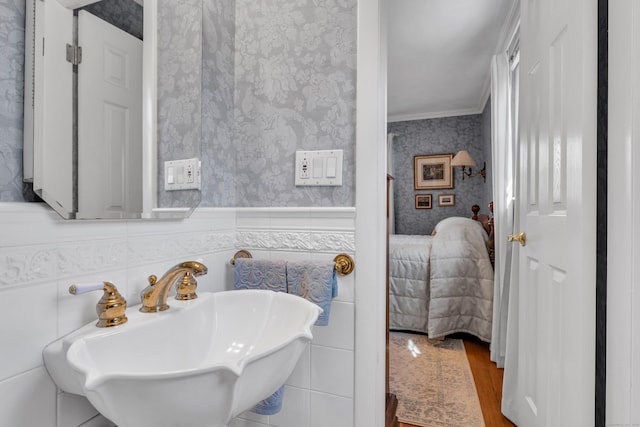 bathroom with wallpapered walls, crown molding, a sink, and wainscoting