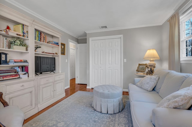 living area featuring baseboards, wood finished floors, visible vents, and ornamental molding