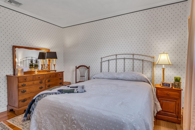 bedroom featuring visible vents, wallpapered walls, and wood finished floors