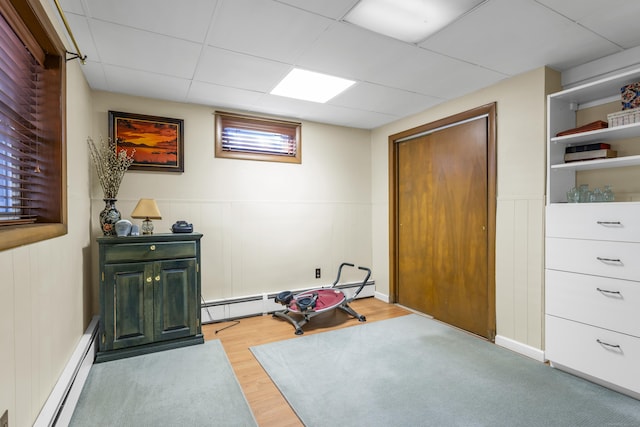 exercise area featuring a baseboard heating unit, wood finished floors, a paneled ceiling, and baseboard heating