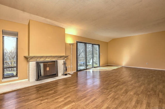 unfurnished living room featuring a textured ceiling, wood finished floors, baseboards, vaulted ceiling, and a brick fireplace