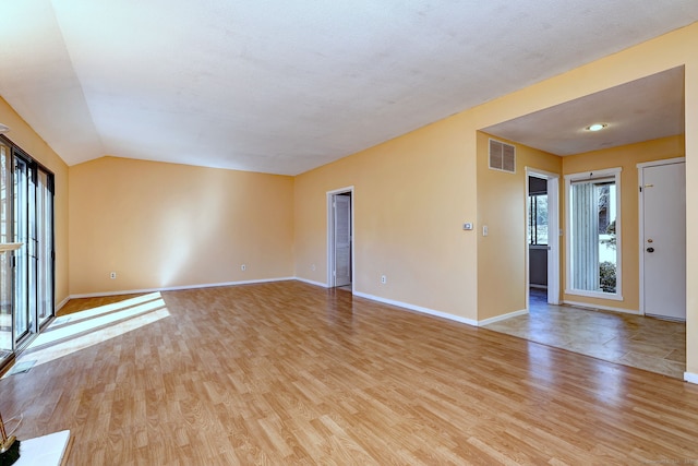 spare room featuring light wood-type flooring, baseboards, visible vents, and lofted ceiling