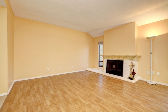 unfurnished living room featuring lofted ceiling, a brick fireplace, baseboards, and light wood finished floors