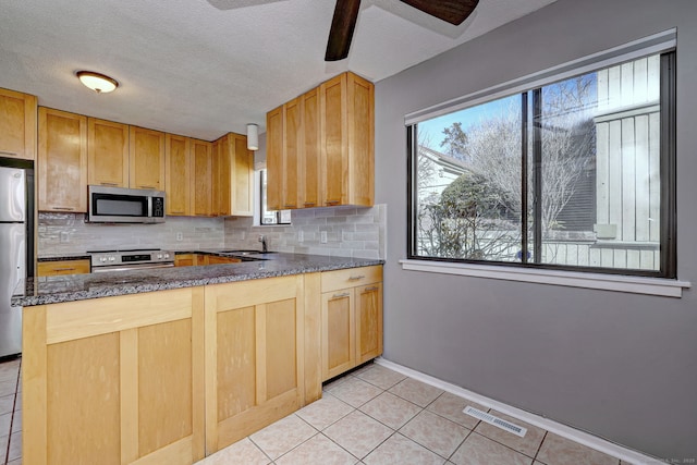 kitchen with light tile patterned floors, stainless steel appliances, a peninsula, visible vents, and backsplash