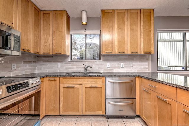 kitchen with decorative backsplash, appliances with stainless steel finishes, light tile patterned flooring, a sink, and dark stone counters