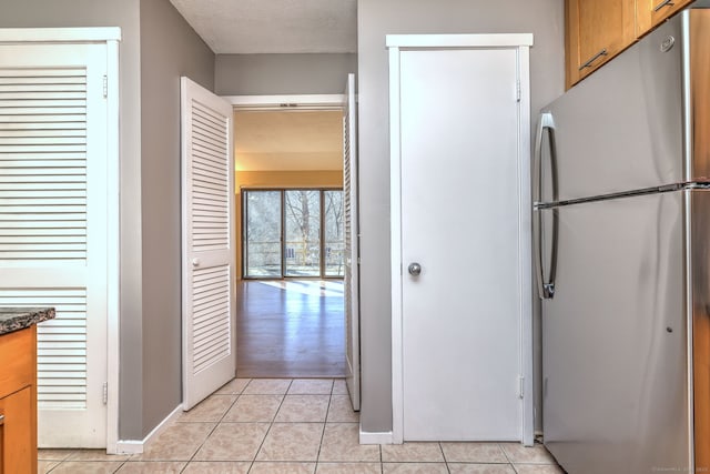 kitchen featuring freestanding refrigerator, brown cabinets, a textured ceiling, and light tile patterned floors