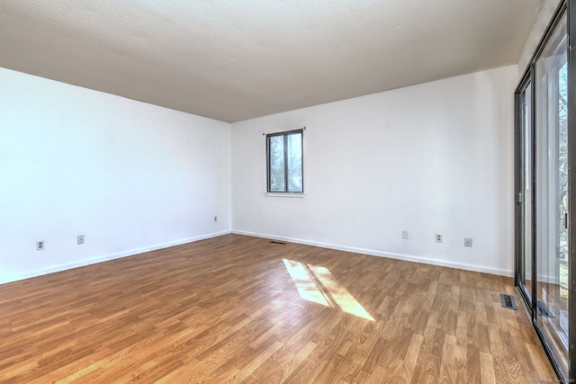 spare room featuring light wood-type flooring, baseboards, visible vents, and a textured ceiling