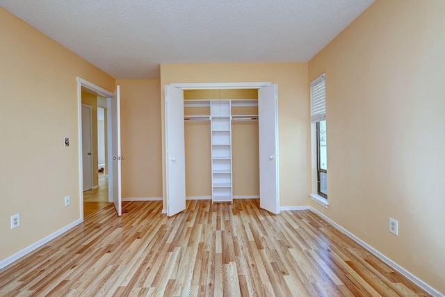 unfurnished bedroom with light wood-type flooring, a closet, baseboards, and a textured ceiling