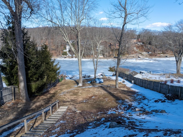 snowy yard with a wooded view and fence