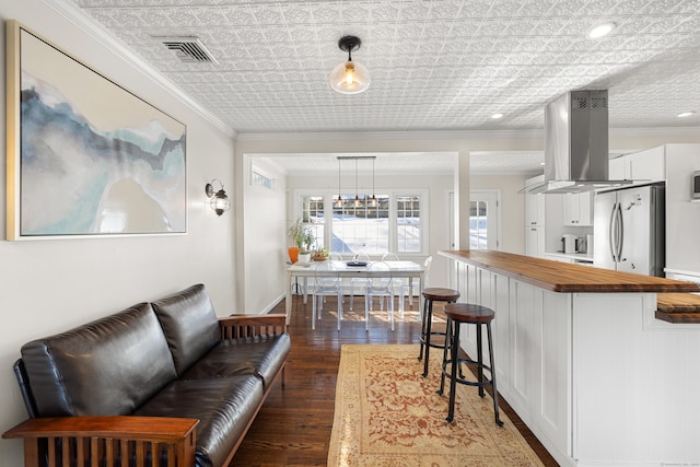 kitchen featuring island exhaust hood, butcher block counters, freestanding refrigerator, white cabinets, and a kitchen bar