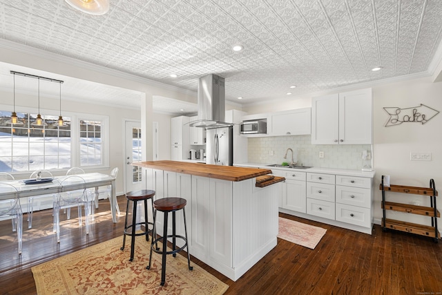 kitchen featuring island range hood, butcher block counters, appliances with stainless steel finishes, a breakfast bar, and a sink