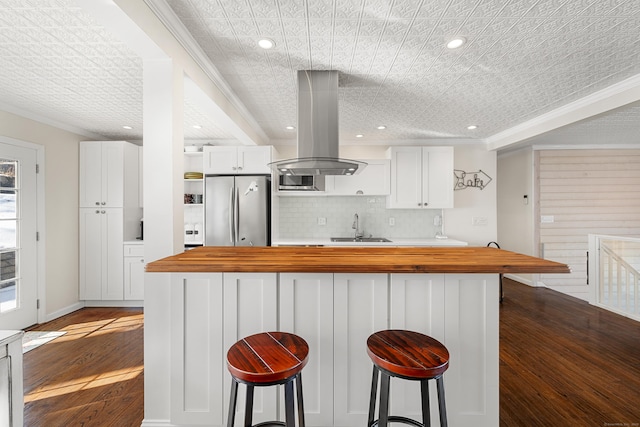 kitchen with wooden counters, freestanding refrigerator, white cabinets, a sink, and island range hood